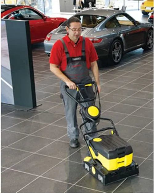 Man using the Tornado BR 16/3 Compact Floor Scrubber in a car dealership, efficiently cleaning the showroom floor around vehicles and in tight spaces.