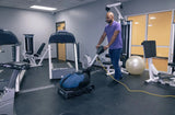Man using the Powr-Flite CAS16 compact cylindrical brush scrubber to clean the floor in a gym, demonstrating the machine's efficiency and ease of use in maintaining clean and safe workout areas